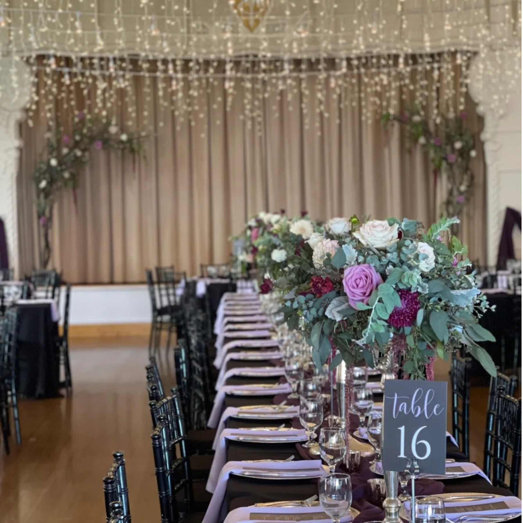 Ballroom wedding reception with black chiavari chairs, purple linens, and lush floral centerpieces