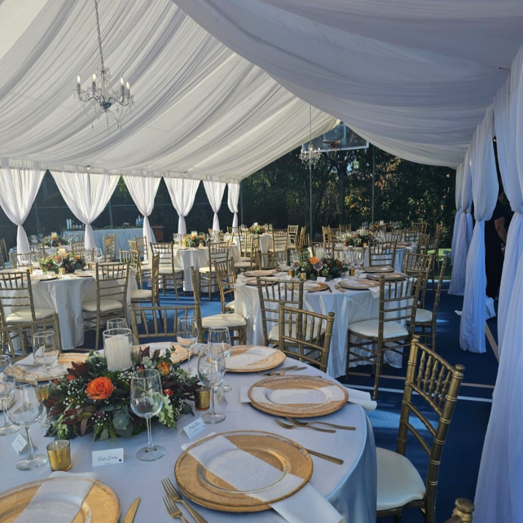 Draped tent wedding reception with gold chiavari chairs, rattan chargers, and fall floral centerpieces