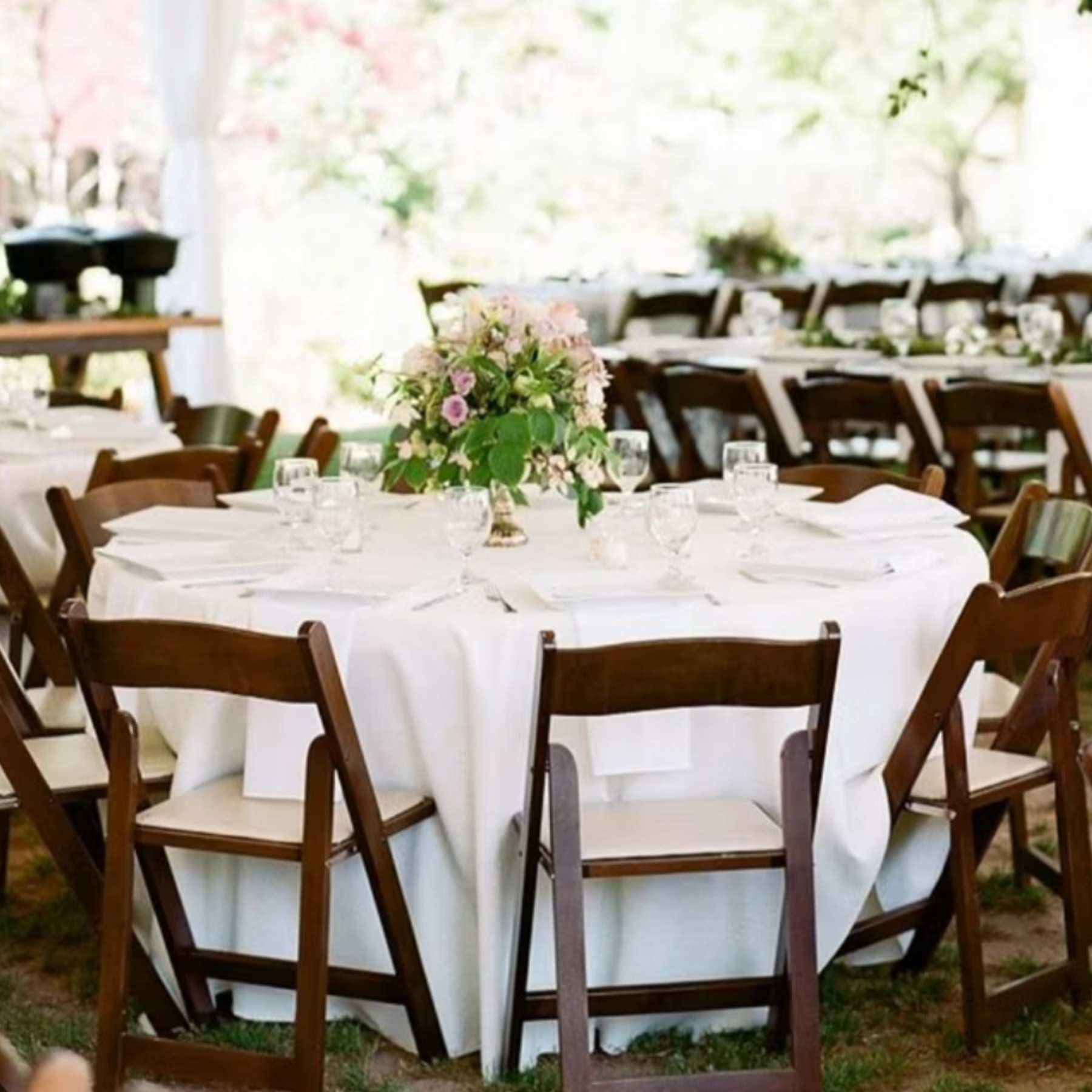 Outdoor tent wedding reception with fruitwood chairs and floral centerpieces