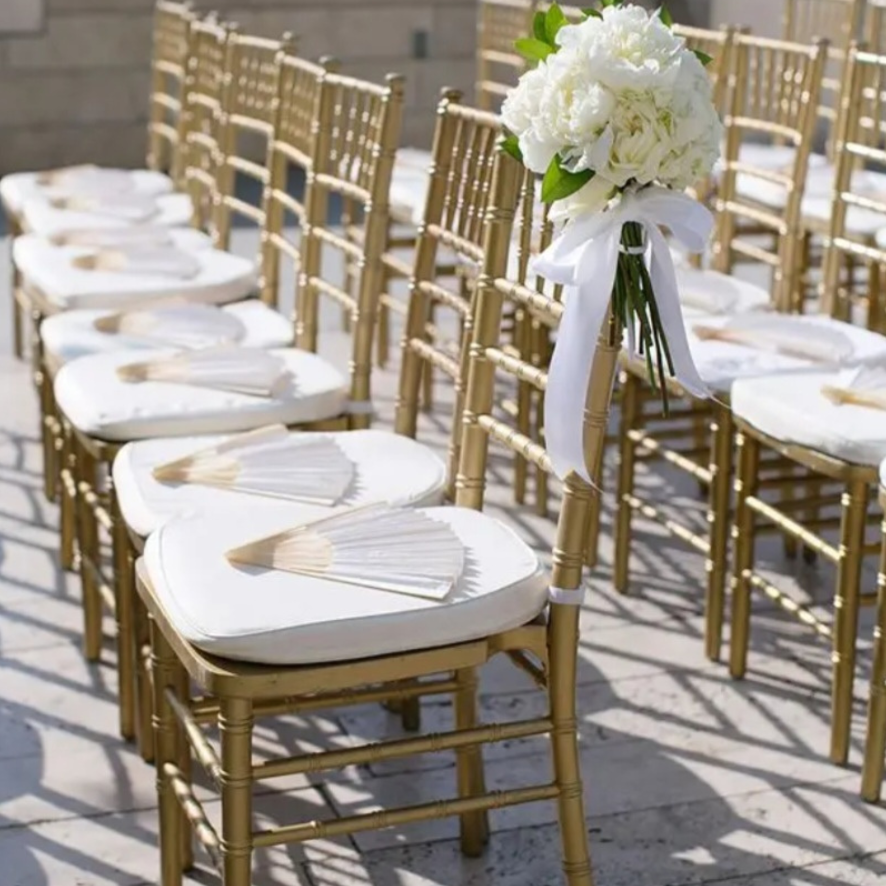 Outdoor ceremony aisle lined with gold chiavari chairs and white floral bouquets