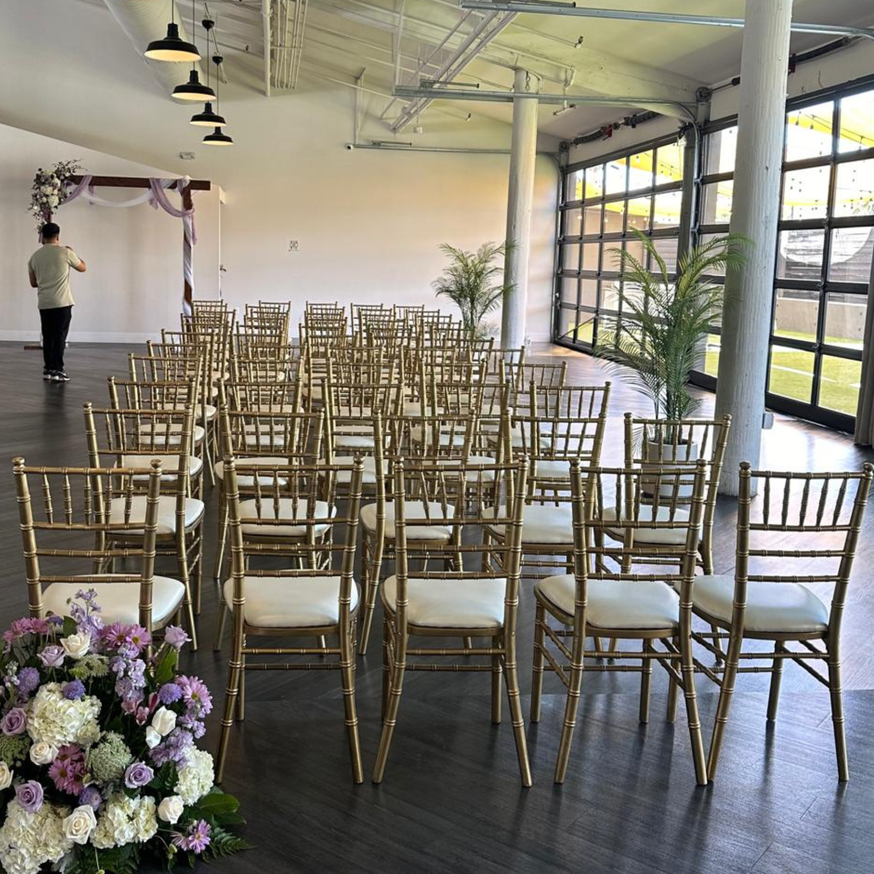 Indoor ceremony with gold chiavari chairs, floral arch, and modern industrial venue