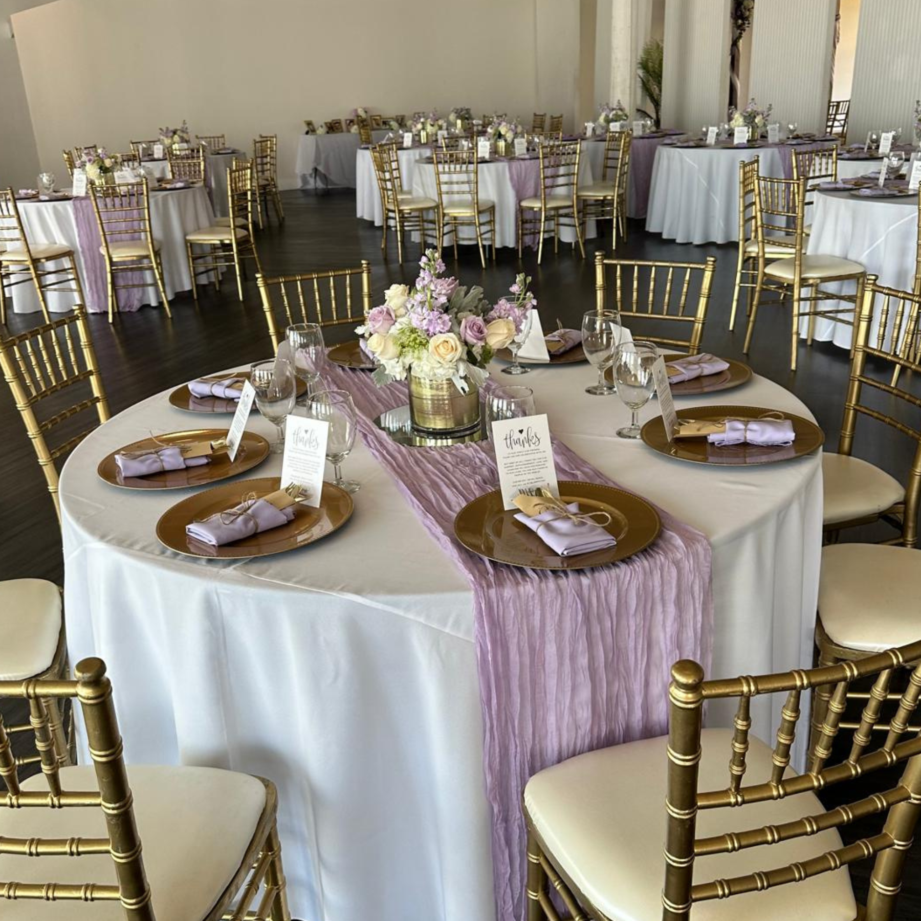 Elegant reception with gold chiavari chairs, white linens, lavender cheesecloth runners, and gold chargers