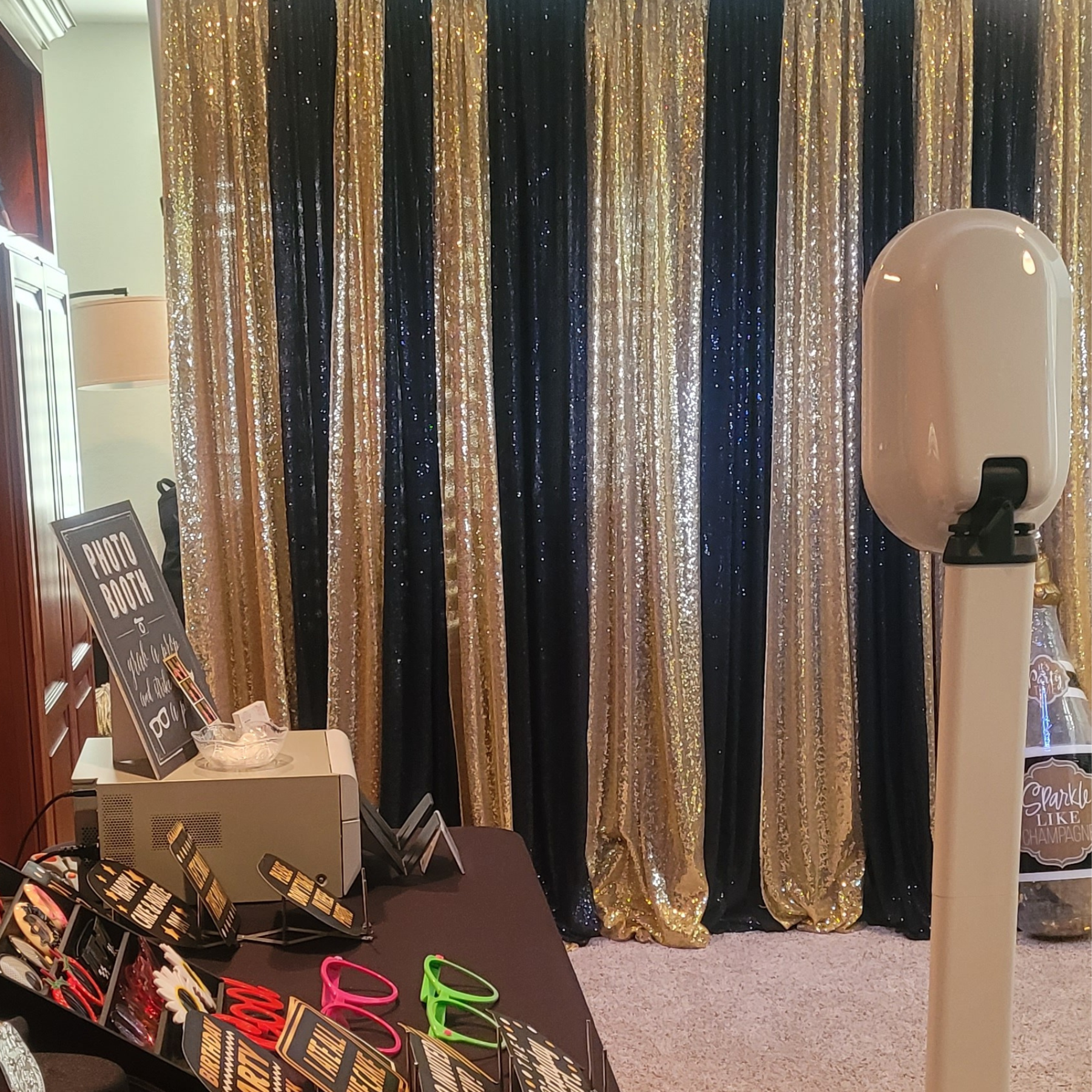 Photo booth setup with gold and black sequin backdrop and props