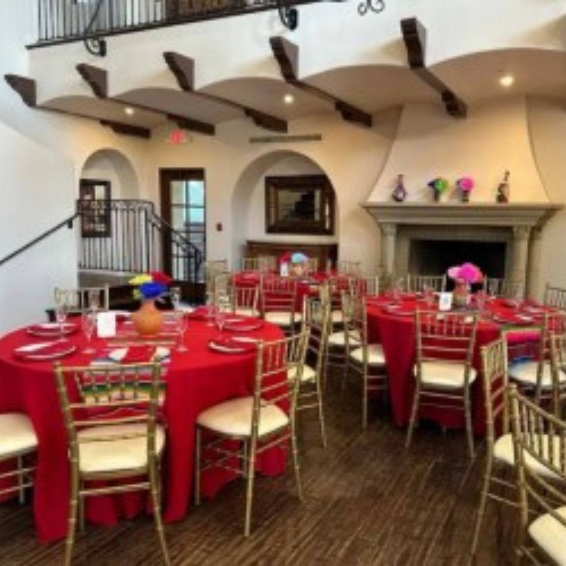 Elegant event venue with red linens, gold chiavari chairs, and colorful floral centerpieces