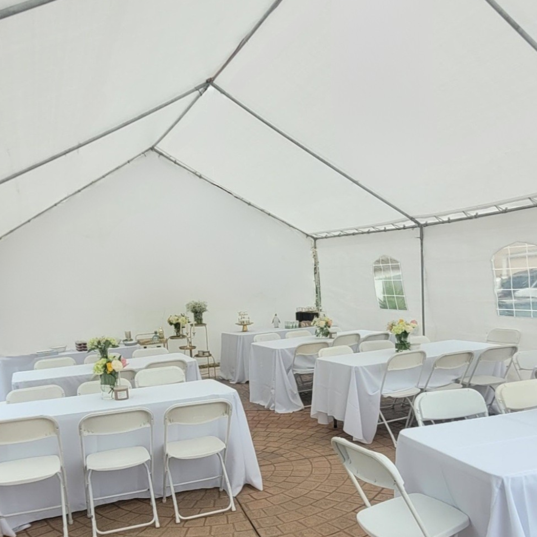 Elegant tent event setup with white rectangular tables, folding chairs, and floral centerpieces
