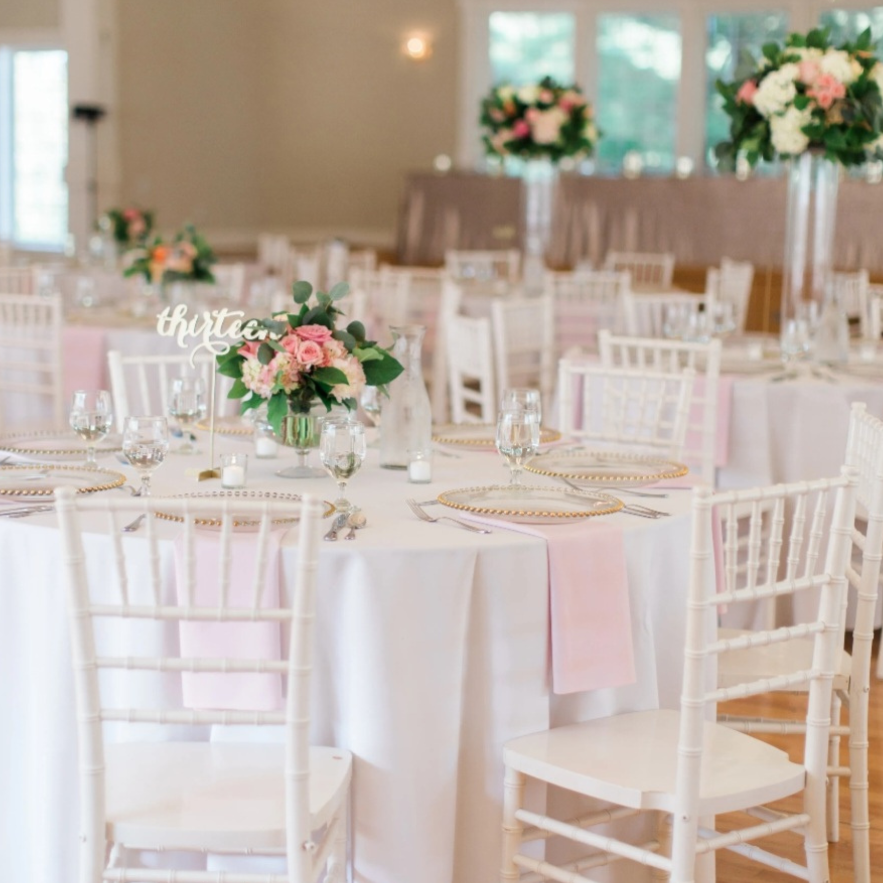 Elegant reception with white chiavari chairs, pink floral centerpieces, and gold chargers