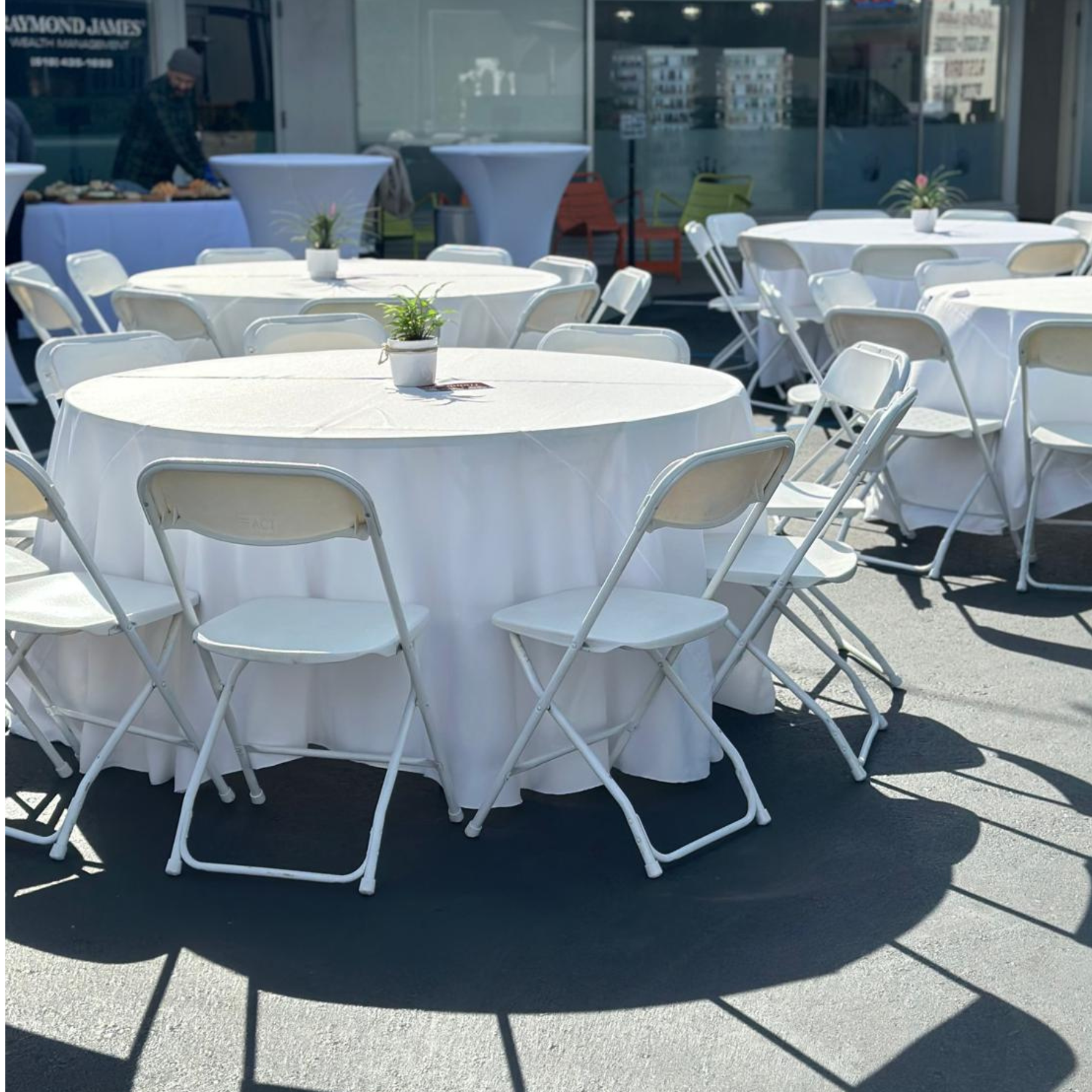 Outdoor event setup with white folding chairs and round tables with linens