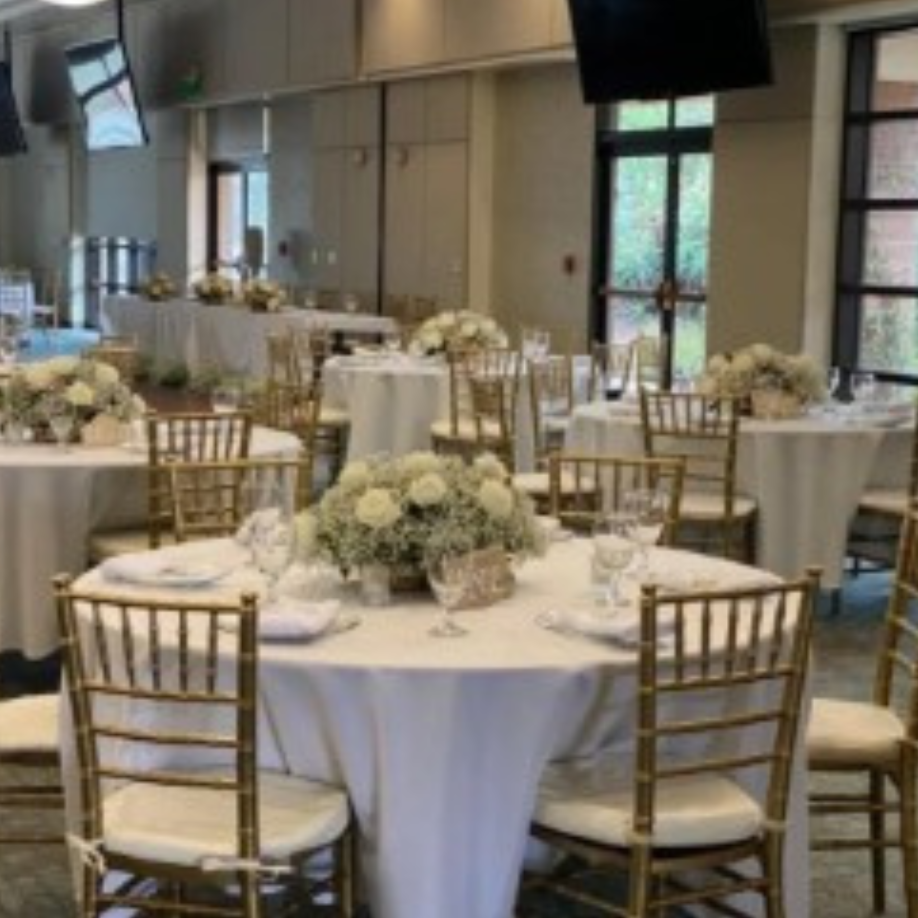 Wedding reception with white linens, gold chiavari chairs, and lush white floral centerpieces